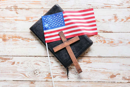 Holy Bible with cross and flag of USA on light wooden background