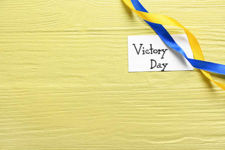 Card with text VICTORY DAY and ribbons in colors of Ukrainian flag on yellow wooden backgroundの写真素材
