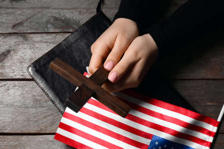 Woman with cross, Holy Bible and USA flag on dark wooden background, closeupの写真素材