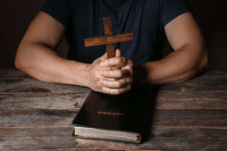Man with cross and Holy Bible on dark wooden backgroundの写真素材
