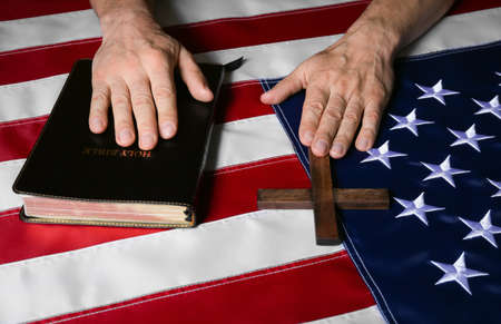Man with Holy Bible and cross on USA flag, closeupの写真素材