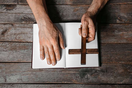 Man with cross and open Holy Bible on dark wooden backgroundの写真素材