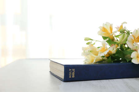 Holy Bible with lily flowers on table in roomの写真素材