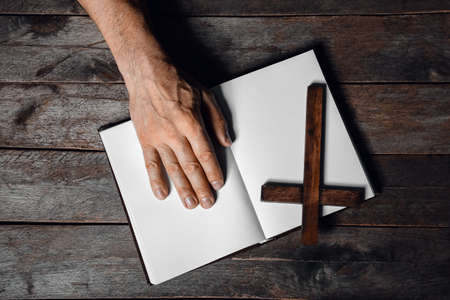 Man with cross and open Holy Bible on dark wooden backgroundの写真素材
