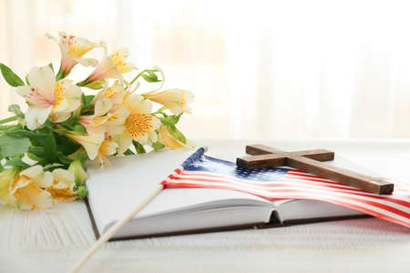 Holy Bible with cross, flowers and USA flag on table in roomの写真素材