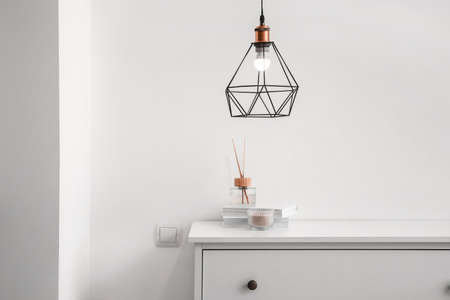 Reed diffuser with books on shelf and glowing lamp near white wallの写真素材