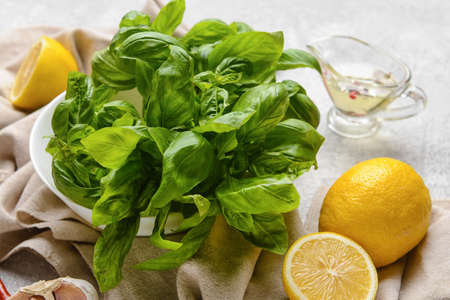 Fresh basil leaves, lemons and oil on light background