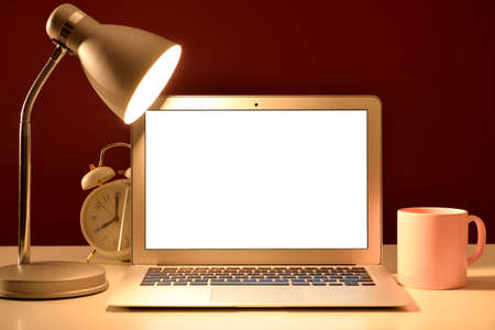 Stylish comfortable workplace with modern laptop and glowing lamp in the eveningの写真素材