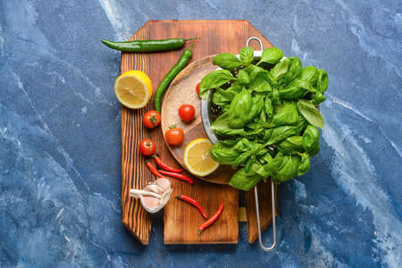 Colander with fresh basil leaves and different products on color background