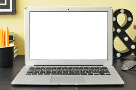 Modern laptop on dark table near color wall