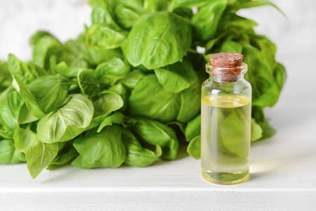 Fresh basil leaves and bottle of essential oil on light wooden backgroundの写真素材