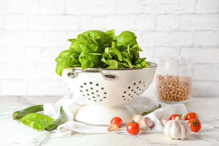 Colander with fresh basil leaves and different products on table against brick wallの写真素材