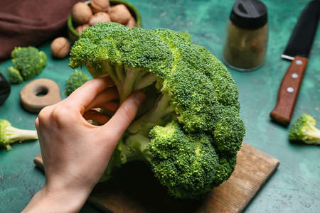 Female hand with healthy broccoli cabbage on color backgroundの写真素材