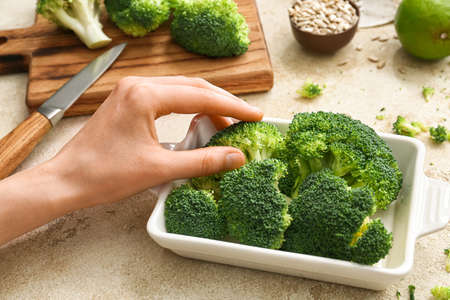 Female hand with healthy broccoli cabbage on light backgroundの写真素材