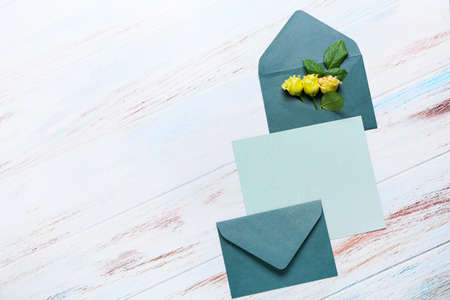 Blank card with envelopes and roses on white wooden background