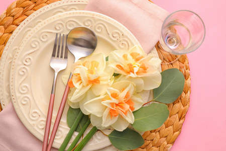 Beautiful table setting with narcissus flowers on color background