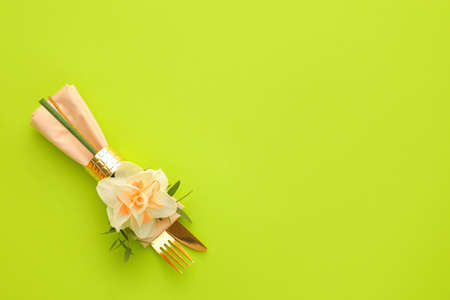 Stylish cutlery with napkin and narcissus flower on color backgroundの写真素材