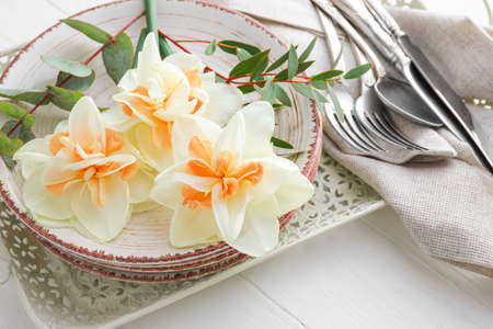 Beautiful table setting with narcissus flowers on light wooden backgroundの写真素材
