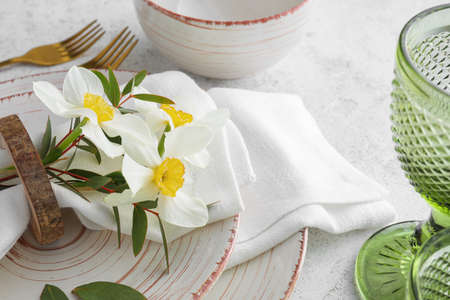 Beautiful table setting with narcissus flowers on light background
