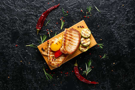 Board with tasty grilled vegetables and steaks on dark backgroundの写真素材