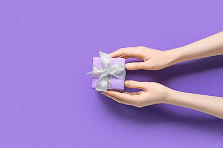 Woman holding gift box on color backgroundの写真素材