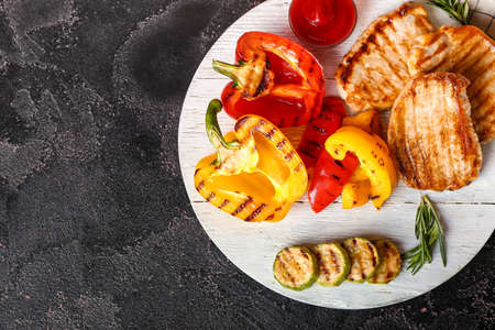Board with tasty grilled vegetables and steaks on dark background