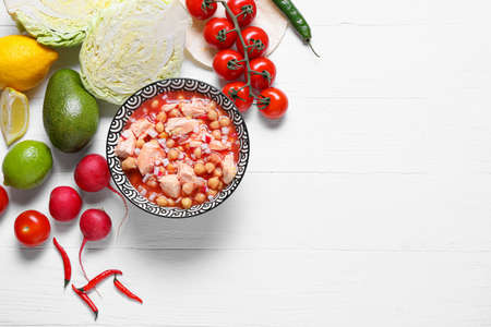 Bowl with tasty pozole soup and ingredients on light wooden background