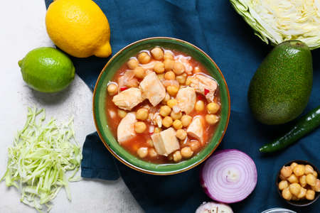 Bowl with tasty pozole soup and ingredients on light background