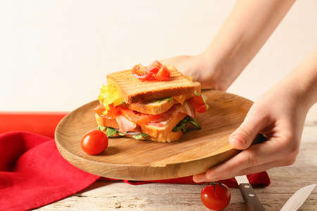 Woman holding plate with tasty sandwich, closeup