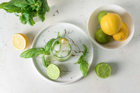 Glass of lemonade with basil on light background