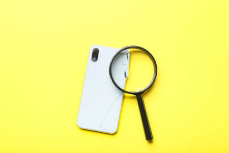 Broken mobile phone and magnifier on yellow backgroundの写真素材