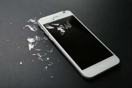 Mobile phone with broken screen and pieces of glass on dark background, closeupの写真素材