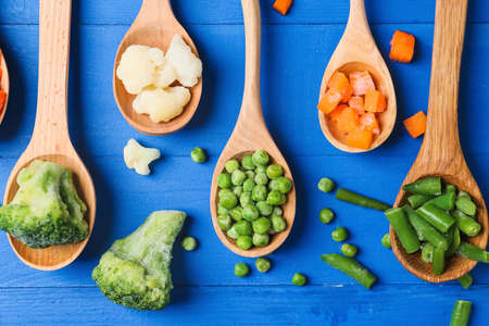 Spoons with different frozen vegetables on color wooden background, closeupの写真素材