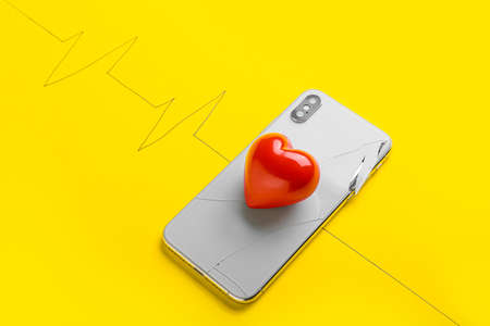 Damaged mobile phone, red heart and drawn cardiogram on yellow backgroundの写真素材