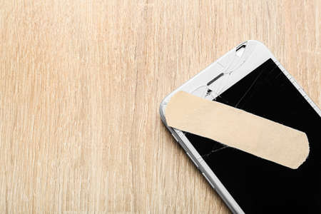 Mobile phone with broken screen and medical plaster on wooden background, closeupの写真素材