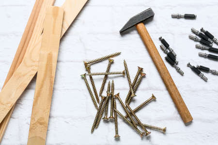 Wooden plank, hammer, screws and bolts on white brick background