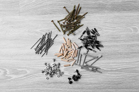 Piles of different bolts, screws, nails, dowels and pins on gray wooden background