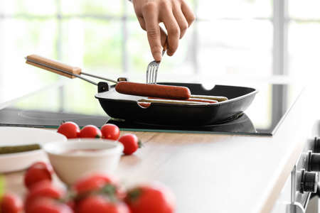 Young man frying tasty sausages in the kitchenの写真素材