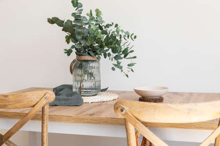 Dining table with eucalyptus branches in vase near light wallの写真素材