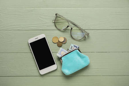 Wallet with money, eyeglasses and mobile phone on green wooden background