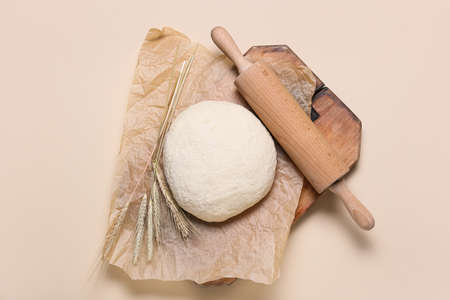 Raw dough with rolling pin on light background