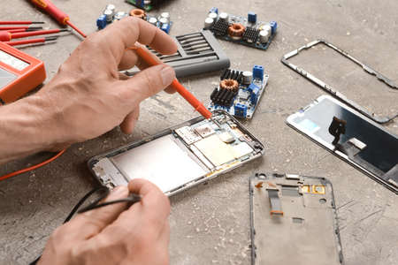 Male technician repairing damaged mobile phone on grunge background
