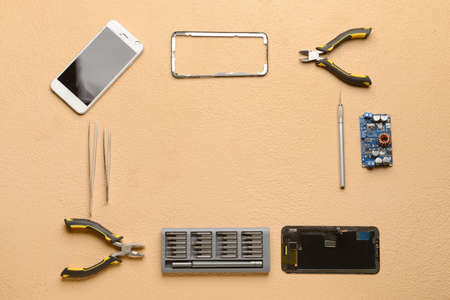 Frame made of damaged mobile phones with technician tools on color background