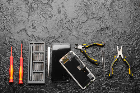 Disassembled mobile phone with technician tools on dark backgroundの写真素材