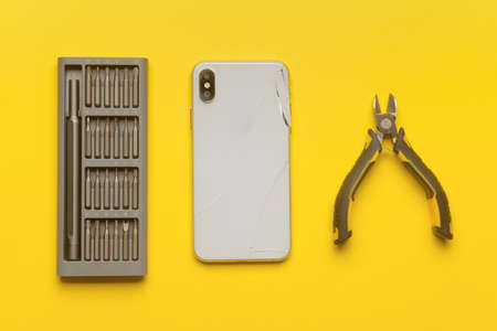 Damaged mobile phone with technician tools on color backgroundの写真素材