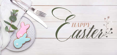 Plate with tasty Easter cookies in shape of bunny on white wooden background