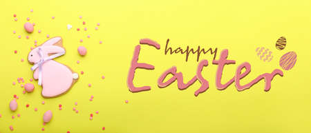 Tasty Easter cookie in shape of bunny and sprinkles with candies on yellow background
