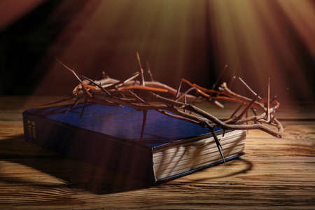 Holy Bible and crown of thorns on table against dark background
