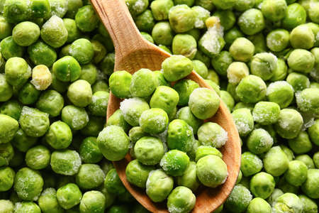 Spoon with frozen green peas as background
