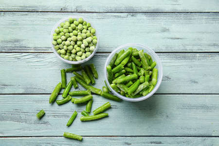 Containers with frozen green peas and beans on color wooden backgroundの写真素材